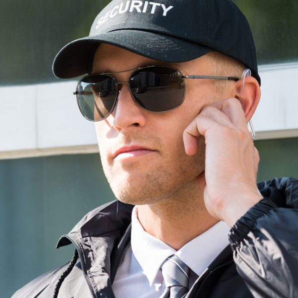 A security personnel in cap and sunglasses, communicating via an earpiece